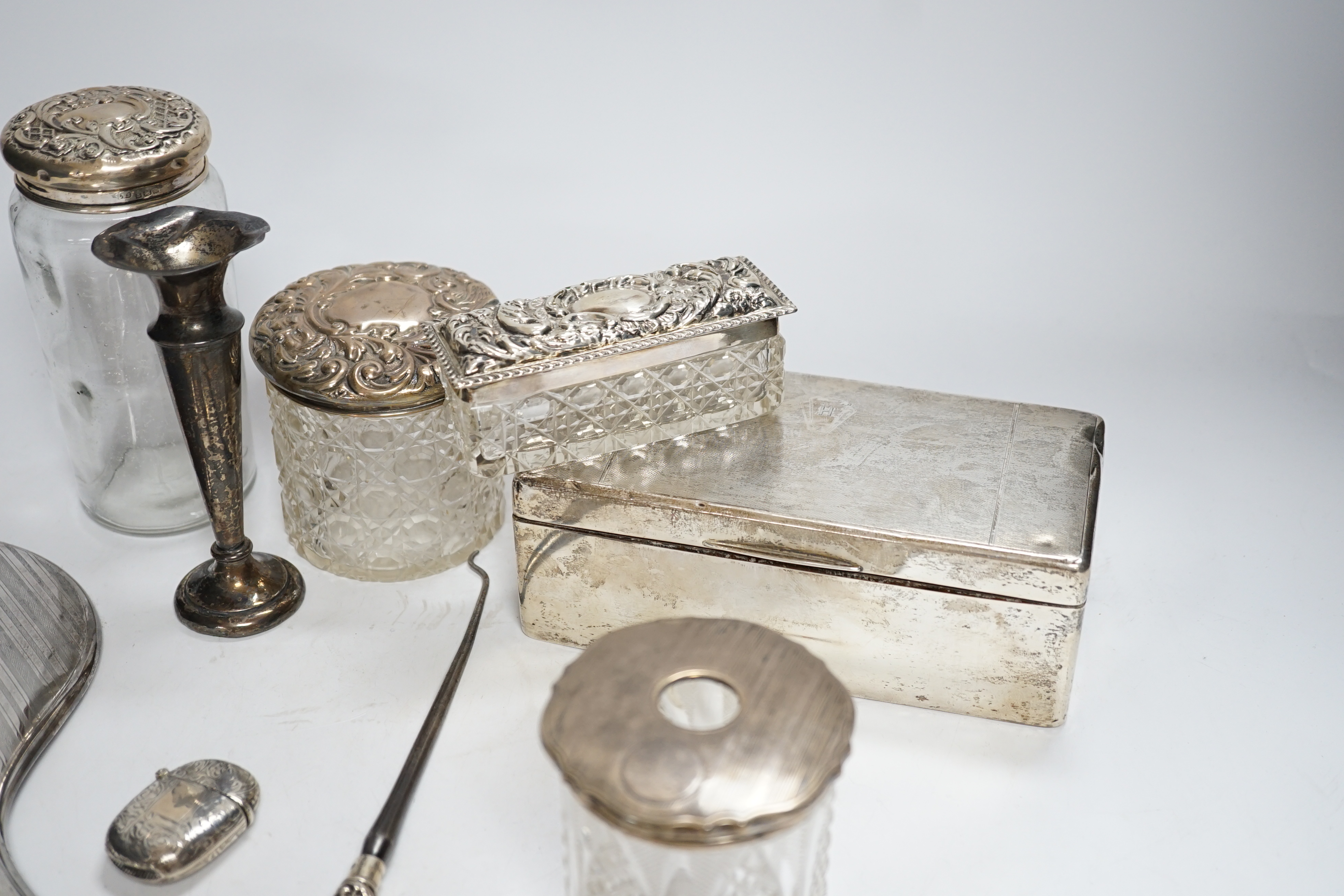 Sundry small silver including a silver mounted cigarette box, four assorted mounted glass toilet jars, a vesta case, button hook, hand mirror and trumpet vase.